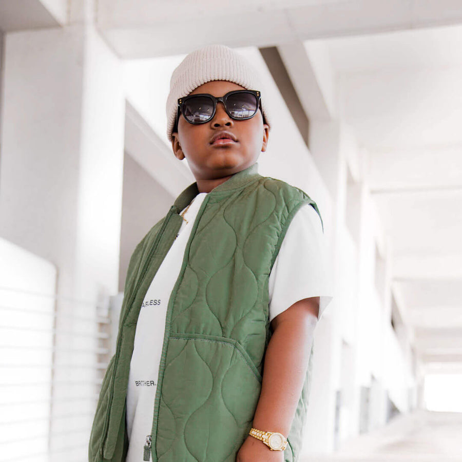 A boy standing posing looking formidable while wearing his black toucca kids sunglasses